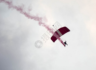 在空中展览期间 剪影降落伞特技在空中滑行时没有聚焦和模糊 带着红色的烟雾痕迹活动飞机空气危险日落冒险翅膀红烟男人运动图片