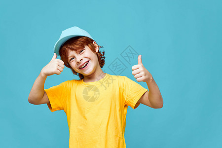 穿着蓝帽子的红发男孩在黄色T恤笑容上露出拇指图片