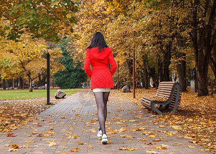 穿着红色大衣的年轻女孩在巷子里走着森林季节晴天外套黄色胡同女士公园树叶天气图片