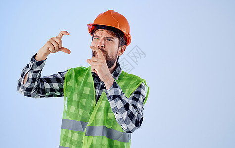 穿着硬帽子的情感建筑师 和反感怜悯的姿态 他的双手在蓝背景上建造建设者工人工具安全帽职业衬衫男人头盔男性图片