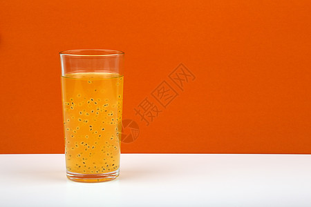 在橙色背景和文字空间的白桌上 有鲜果汁及激情果子种子的新鲜果汁图片