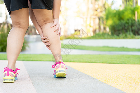 女性胖脚步运动员腿部受伤和疼痛 手抓着痛苦的腿在公园里跑来跑去事故踪迹赛跑者小牛女士十字形疾病伤害治疗抽搐背景图片