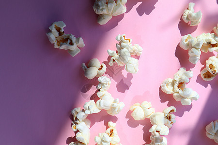 分散在粉红色背景上的爆米花流行音乐美味电影工作室说谎食物小吃剧院娱乐黄油图片