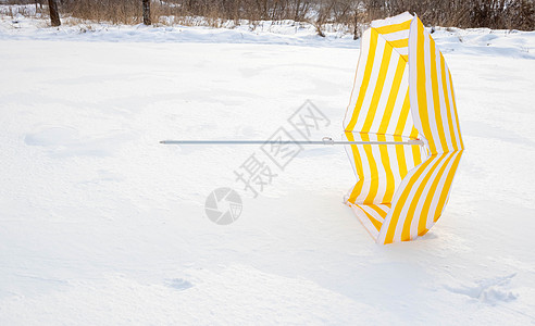 白雪上坠落的黄色浅黄条纹海滩雨伞 在一片被雪覆盖的空旷地带公园中的白雪中地面日历环境草地气候场景旅行天气问候气象图片