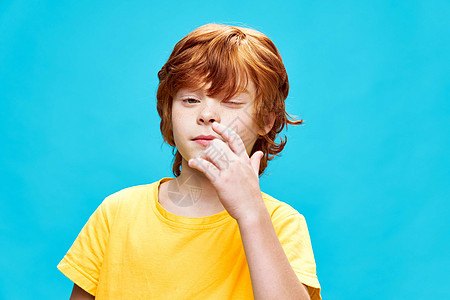 紧闭眼睛的红头发男孩在鼻子附近用手指着黄色T恤衫图片