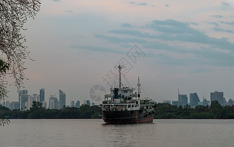 一艘货轮在晚上停泊在Chao Phraya河中部 背景是绿林和摩天大楼货船货运天空地平线首都戏剧性城市巡航乘客船舶图片