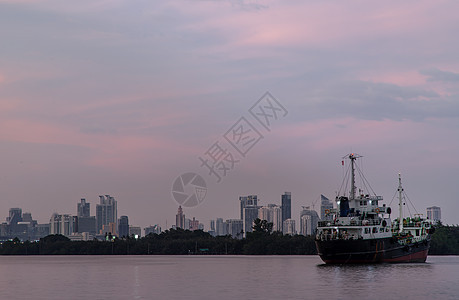 一艘货轮在晚上停泊在Chao Phraya河中部 背景是绿林和摩天大楼市中心血管场景船舶戏剧性商业乘客首都森林船运图片