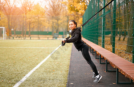 女运动员在运动场上训练 混血年轻成年女性使用悬挂系统进行锻炼 健康的生活方式 伸展户外游乐场体质操场肌肉吊带女孩活动公园运动装女图片