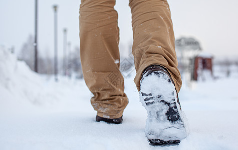 一个人在滑滑的路上行走 在公园里第一次下雪踪迹步伐运动鞋类雪花旅行季节衣服皮革天气图片