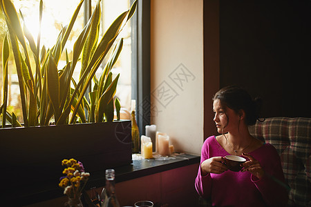 年轻的黑发美女在温馨的咖啡厅里向窗外望去图片