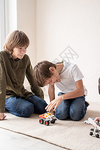 年轻男孩玩得开心 坐在地毯上制造机器人汽车图片