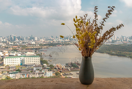 陶瓷花瓶中的干花在阳台的木桌上手工制作 享有城市景观背景图片