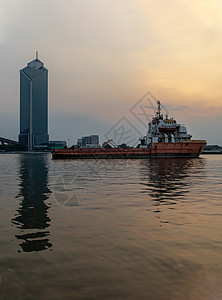 一艘货轮在晚上停泊在Chao Phraya河中部 其背景是现代建筑船舶巡航货运蓝色首都戏剧性天际血管货船地平线图片