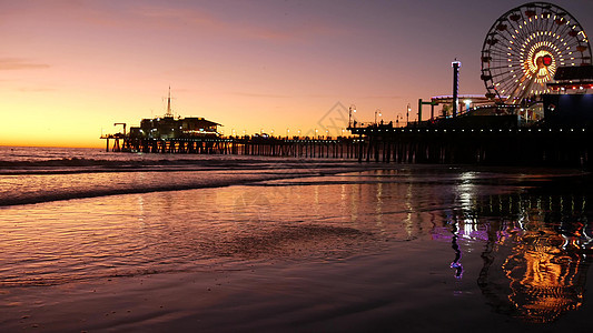 暮光之城波浪映衬着经典的灯光摩天轮 圣塔莫尼卡太平洋海滩度假村码头上的游乐园 加利福尼亚州的夏季标志性符号在黄昏时分发光 美国加图片