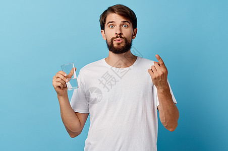 在蓝色背景白色T恤衫模型作物风景上手握着一杯水的长胡子男子矿物饮料手指玻璃饮食工作室液体生活营养男性图片