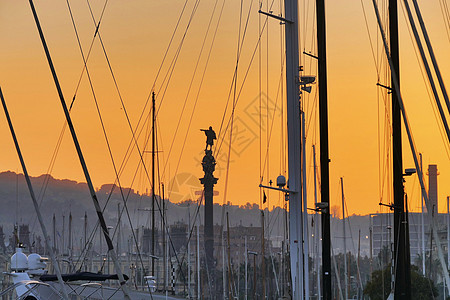 科伦坡雕像环绕光影 通过日落时停泊在港口的船只的树木和护身板图片
