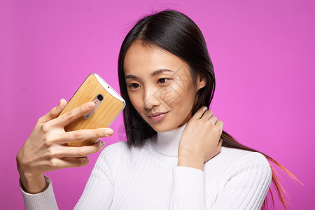 拿着粉红色背景裁剪视图的漂亮女人亚洲外观电话手机喜悦微笑商业女性广告压痛幸福粉色成人图片