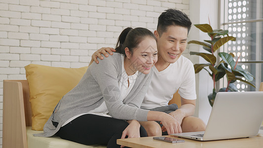 丈夫和妻子在沙发上笑 使用笔记本电脑网络摄像头房子技术互联网微笑女士时间退休母亲恋人幸福图片