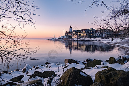 Urk 的冬天 Urk 灯塔旁的堤坝和海滩在冬天被雪覆盖 灯塔旁的日落港口地标房子降雪季节天空天气雪花场景传统图片