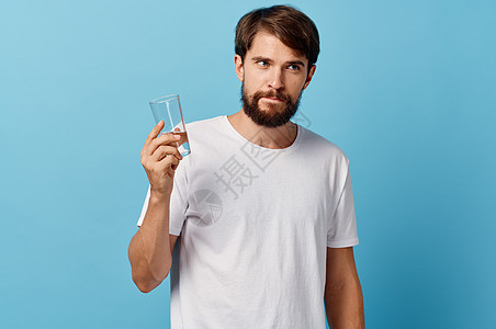 在蓝色背景白色T恤衫模型作物风景上手握着一杯水的长胡子男子工作室男人男性饮料液体口渴营养矿物玻璃手指图片