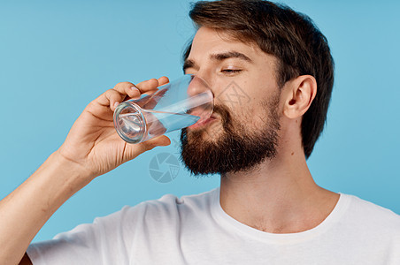 蓝色背景特写肖像画上的玻璃杯中的漂亮男人饮用水 照片来自手指男性矿物健康工作室饮食饮料液体口渴白色图片