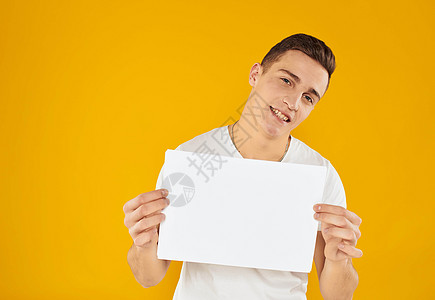 一个穿白色 T 恤的男人 黄色背景上有一张纸模型商务微笑管理人员工作成人卡片广告牌横幅人士广告图片