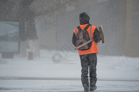 市政服务的一名工作人员带着雪铲在暴风雨 暴风雪或冬季降雪中在城市的恶劣天气中沿着道路行走 北方的极端冬季天气条件气旋风暴薄片季节图片