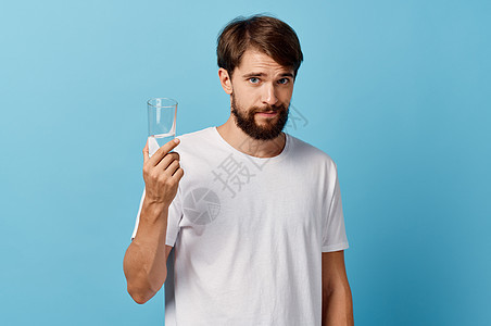 在蓝色背景白色T恤衫模型作物风景上手握着一杯水的长胡子男子营养手指口渴男人矿物男性饮食工作室生活液体图片