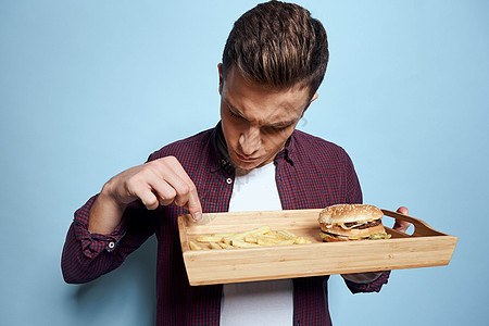 男人穿着衬衫汉堡包 吃蓝背景的薯条图片