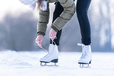 将冬季溜冰的鞋带绑在冰冻湖上 滑冰刀刃乐趣池塘娱乐季节天气溜冰者锻炼冒险女性图片