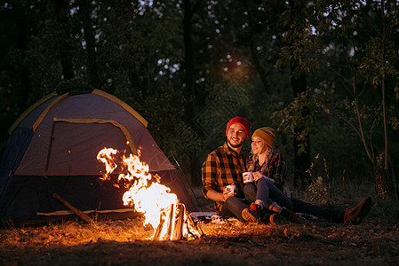一对年轻夫妇 一个男人和一个女孩 戴着漂亮的编织帽子 在露营时停下来了衬衫橙子女孩数字天空温暖胡须蓝色取暖旅行图片