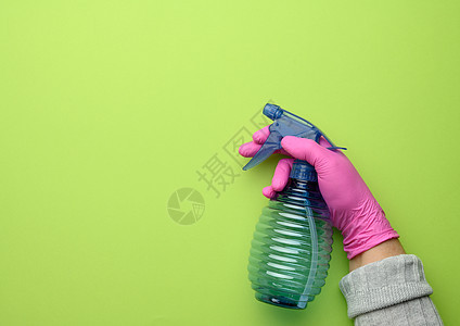 穿粉色手套的女性手持绿色背景的透明塑料喷雾瓶 装在粉色手套上图片