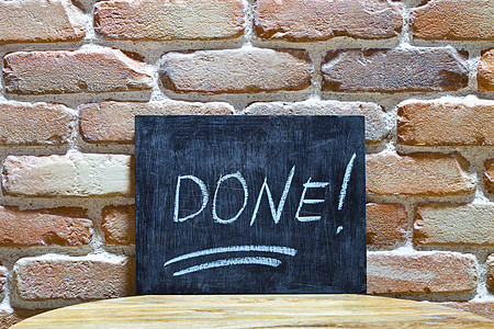 粉笔板上写着DONE的字! 用手和粉笔淹死在砖墙背景上的木制桌子上图片