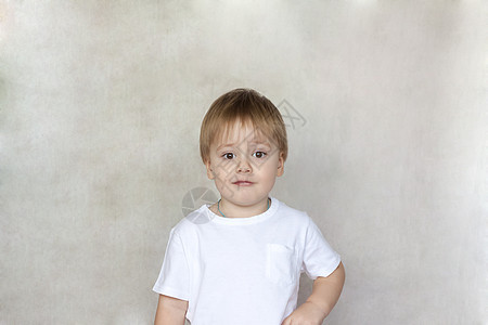 一个穿着白色 T 恤的可爱小男孩的画像 孩子们的情绪 墙上的背景上的孩子 成功 好主意 创意和概念表情微笑男生儿童乐趣童年眼睛图片