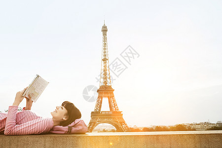 年轻女孩躺在阳台上 在艾菲尔铁塔前读书的图片