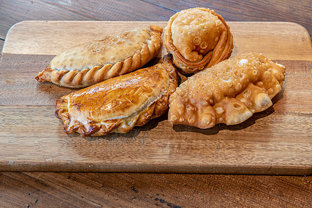在木板上装有不同填料的阿根廷各式瓦纳达馅饼小吃糕点盘子牛肉美食包子面团卷饼面包图片