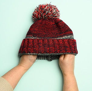手握着冬季编织的红黑帽子 绿色背景上还有蓬蓬图片