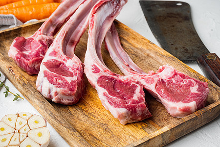 新鲜鲜生肉屠夫羊排牛肉切片 配有胡萝卜橙 草药和旧的屠宰刀子 以白石为背景图片
