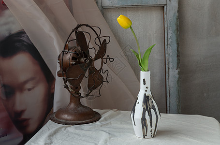 黑白手工陶瓷花瓶中的黄花和复古扇子 在中国古典海报电影框与旧水泥墙前的白色纹理桌布上图片