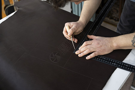男人的手拿着锥子和金属尺子 在他的工作室里制作皮革钱包 与棕色天然皮革的工作过程 工匠拿着制作工具 在皮革上做标记配饰皮艺剪刀成图片