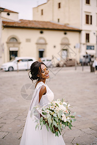 在意大利佛罗伦萨举行的婚礼 穿着白色连衣裙和长面纱的非洲裔美国新娘 新娘捧着华丽的花束婚纱胡子混血皮肤大男子投标花朵街道夫妻绅士图片