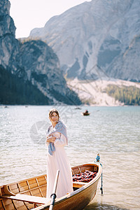 一位新娘站在意大利的木船上 婚礼在欧洲 在 Braies 湖上 一个身穿白色婚纱的年轻女孩 肩上披着一件蓝色毛衣图片
