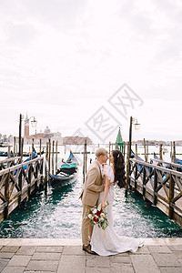 新郎站在贡多拉码头旁 拥抱 在威尼斯 靠近圣马可广场 俯瞰圣乔治马焦雷和落日的天空 意大利威尼斯最大的贡多拉码头棕色玫瑰新娘沙装图片