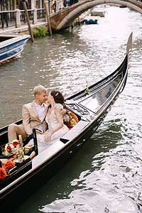 在威尼斯的意大利婚礼上 新娘和新郎骑着经典的木制歌多拉 沿着狭窄的威尼斯运河走幸福玫瑰已婚新婚缆车黑发裙子婚姻合伙传统图片