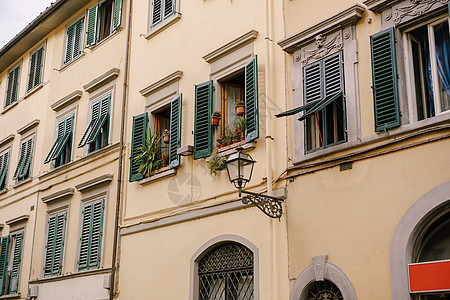 意大利佛罗伦萨一栋公寓楼的外表 上面有绿色木制百叶窗黄色公寓浮雕花盆石头路灯图片