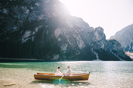 新婚夫妇乘坐木船航行在意大利的 婚礼在欧洲 在 Braies 湖上 新婚夫妇新郎用木桨划船 新娘坐在对面新人恋人幸福夫妻景色已婚图片