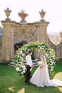 新娘宣读结婚誓言 在意大利托斯卡纳的一座古老的酒庄别墅举行婚礼 意大利古建筑前装饰着白色花朵和绿色植物的圆形婚礼拱门图片