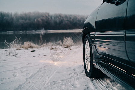 沿河边的黑车黑色汽车 在雪地路上和森林背景上运输暴风雪车轮头灯危险季节车辆天气旅行安全图片