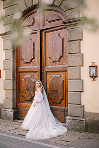 穿着白色大婚纱和长面纱的美丽新娘正站在一个意大利古老恶棍托斯卡纳(佛罗伦萨)的大木制旧门前图片