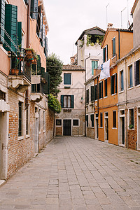 意大利威尼斯建筑立面的特写镜头 死胡同威尼斯人街 五层楼的房子 窗户上有蓝绿色的木百叶窗 窗户上晾干了亚麻布 旧石地板图片